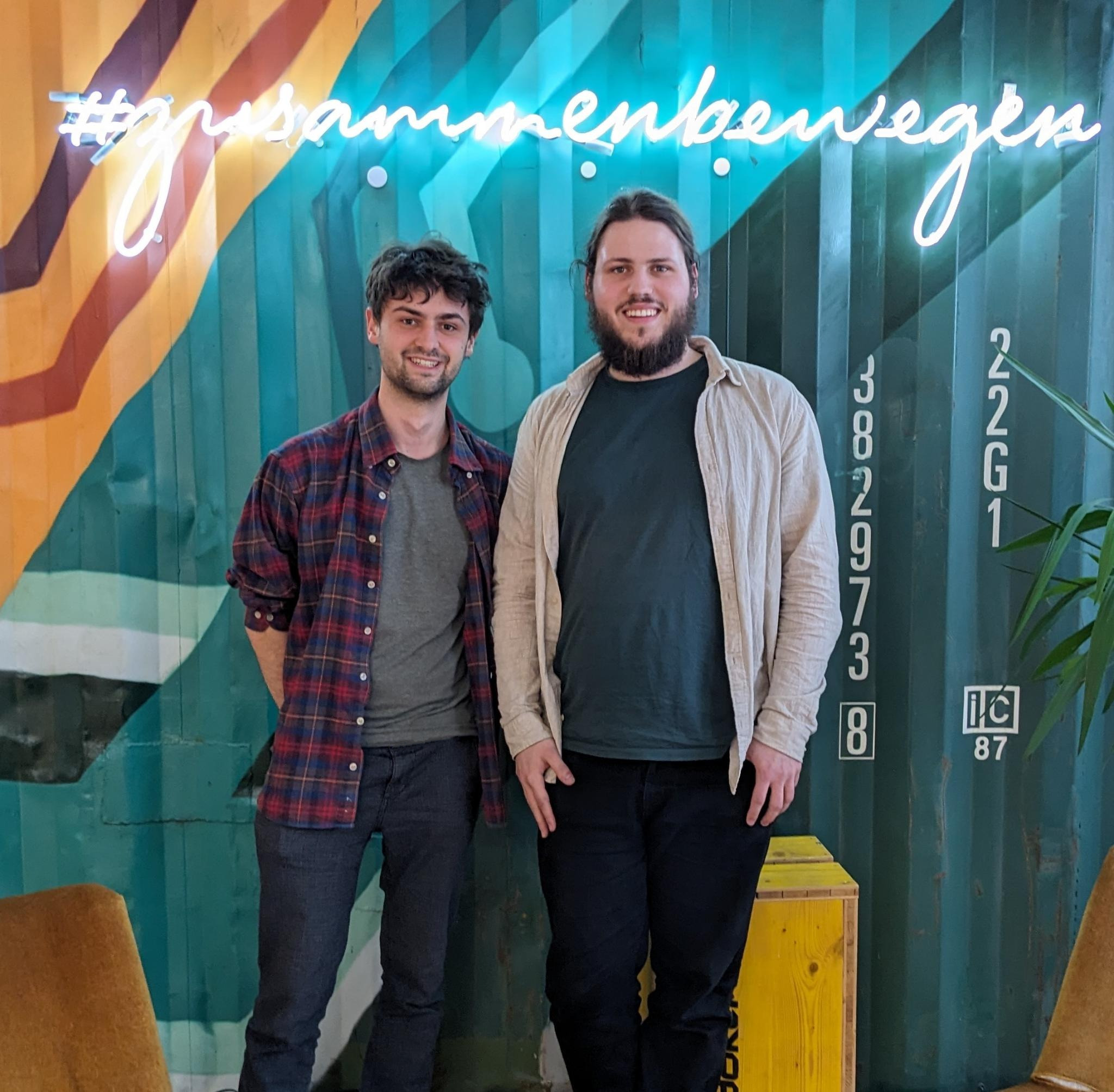 David and Max standing in front of a sign saying #zusammenbewegen